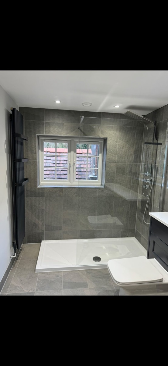 Walk-in shower with grey stone-effect tiles, a chrome shower panel and a black vertical radiator