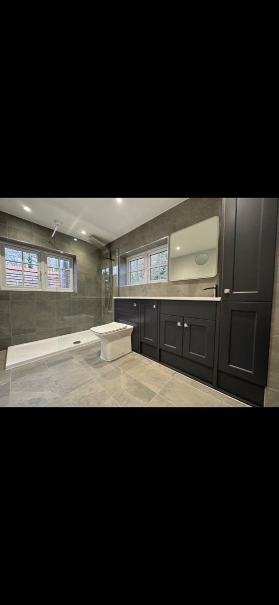 Modern bathroom with grey stone-effect tiles, a walk-in shower, white toilet and black shaker vanity units
