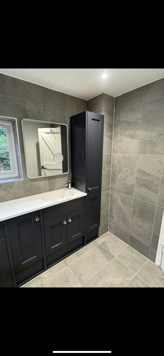 Bathroom vanity with a white basin, black shaker units, a tall cabinet and grey stone-effect tiling
