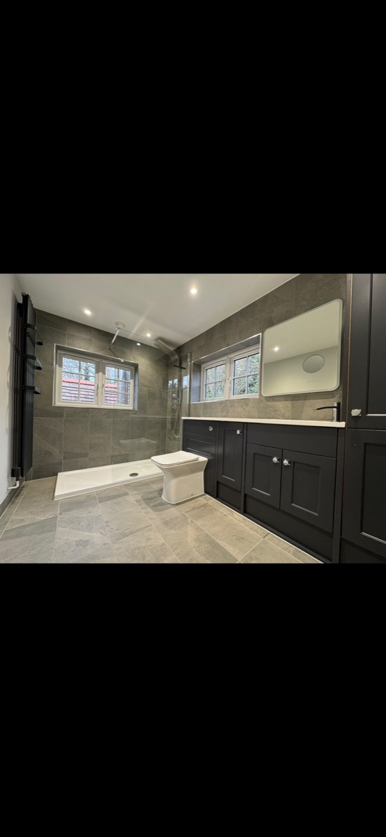 Grey-tiled bathroom with a level-access walk-in shower, white toilet and black vanity units