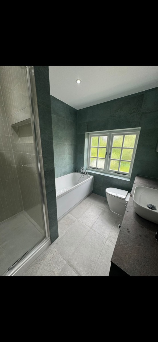 Bathroom with green-grey tiles, a white bath with a chrome mixer tap and a glazed walk-in shower