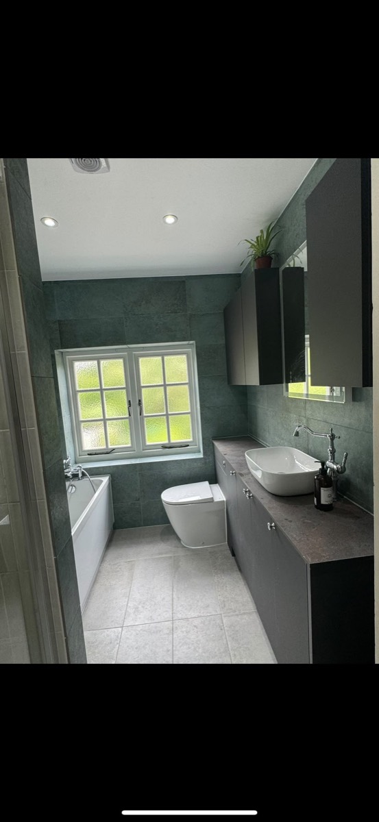 Bathroom with green-grey stone-effect tiles, a white bath, toilet and a grey vanity with a counter-top basin