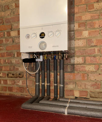 White boiler mounted on an exposed brick wall with neat insulated pipework