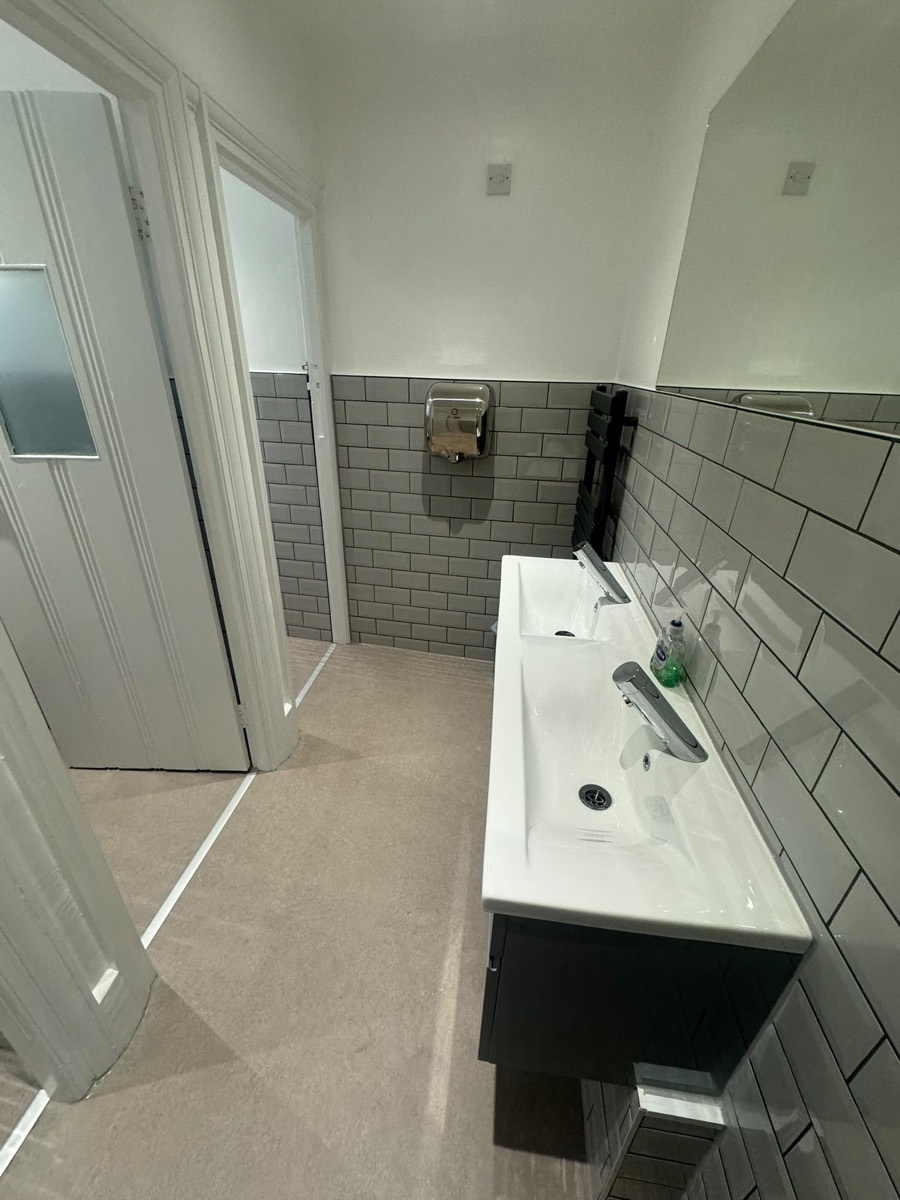 Commercial washroom with a long white double vanity basin, chrome taps and grey metro-tiled walls