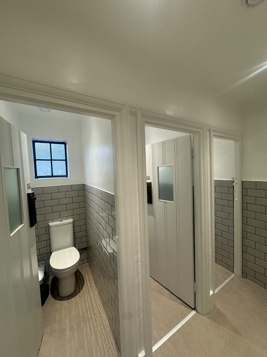 Commercial toilet washroom with white cubicle doors and grey metro-tiled WC cubicles