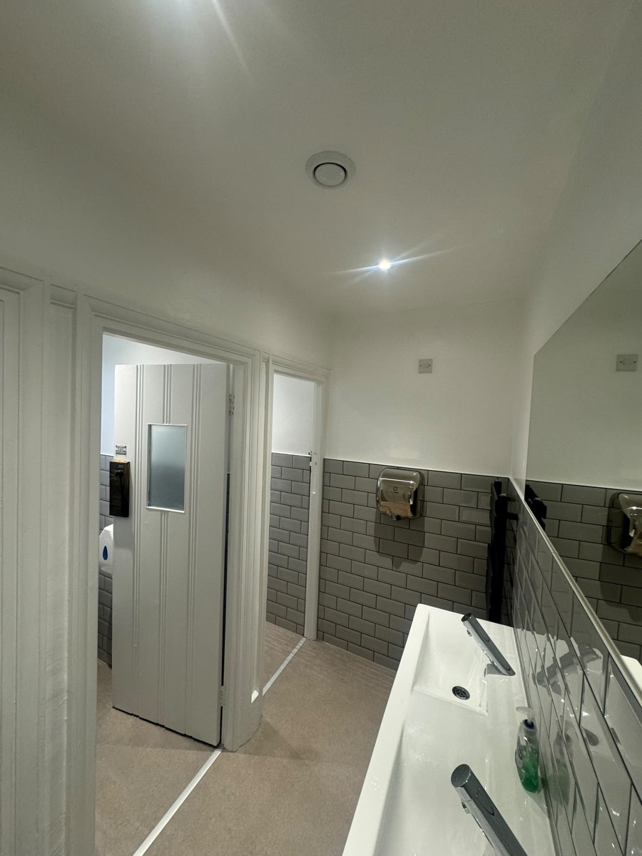 Commercial washroom with twin wall-hung basins, a large mirror and a hand dryer on grey metro tiles