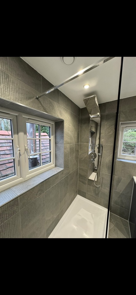 Walk-in shower enclosure with a chrome shower tower and grey stone-effect tiling beside a leaded window
