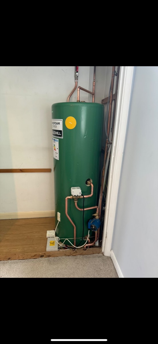 Green Telford hot water cylinder in an airing cupboard with copper pipework, a pump and a motorised valve